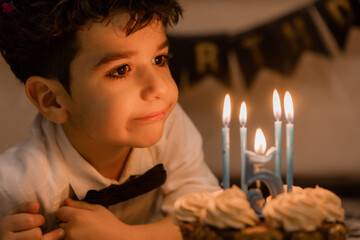 handsome little curly-haired brunette boy makes a wish and blows out the candles on the cake