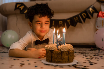 handsome little curly-haired brunette boy makes a wish and blows out the candles on the cake