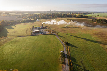 Small factory with smoking chimney in green field, aerial view