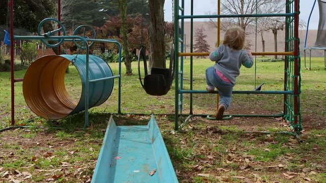 Small toddler girl struggle to climb up the ladder with feet on the colourful playground