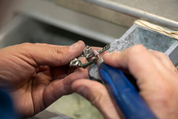 main d'un technicien passant une meule sur un chassis en métal chrome cobalt pour la création d'un bridge dentaire