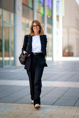 Obraz premium A middle aged businesswoman wearing business casual and walking on the street