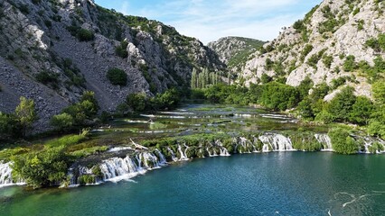Aerial view of a small waterfall between two hills in Croatia. Drone photo 4K. Landscape scenery with a water, hills, bushes and trees.