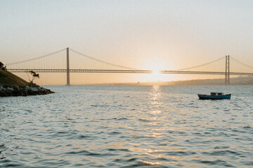 Golden Sunset Behind 25 de Abril Bridge with Boat – Lisbon, Portugal