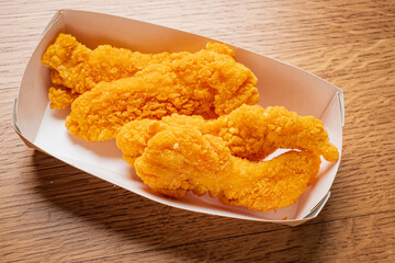 Three perfectly fried chicken tenders are arranged neatly in a takeout box, ready to be enjoyed