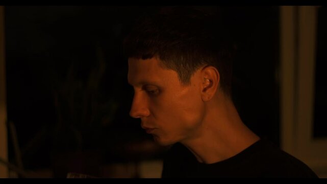 Lonely alcoholic sipping bourbon at home closeup. Young man holding whiskey glass drinking alcohol at evening interior. Melancholic hopeless man suffering after breakup alone