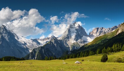 picturesque alpine landscape with high mountain peaks and green grass meadow against a blue cloudy sky
