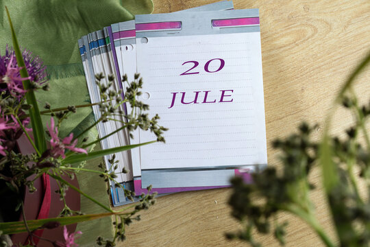 Calendar for July 20: numbers 20, name of the month July in English on a flip calendar among flowers