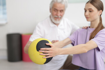 Doctor and patient exercising with medicine ball in clinic, selective focus