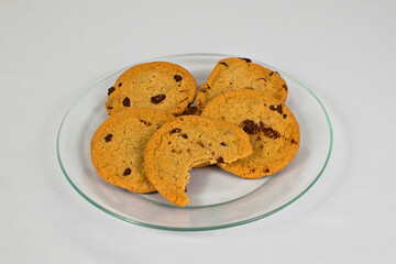 A plate of chocolate chip cookies, one partially eaten, sits on a white surface, perfect for a snack or dessert.