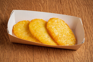 Three crispy potato cakes in a simple container highlight their golden perfection