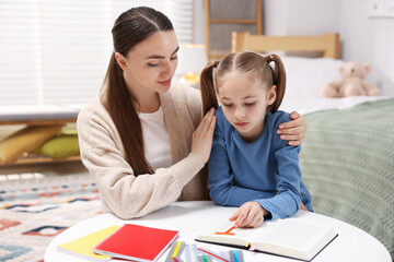 Dyslexia. Mother and her daughter reading book at table indoors