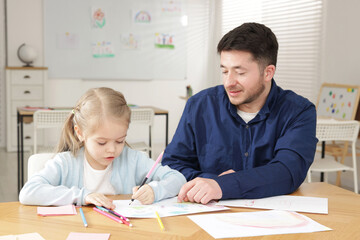 Little girl drawing during lesson with teacher at desk indoors