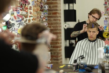 Professional barber cutting client's hair with scissors in barbershop, selective focus