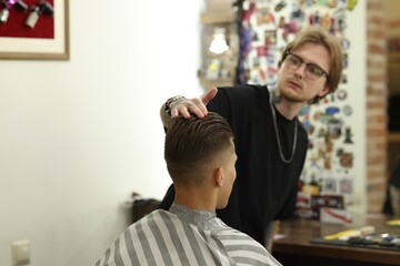 Professional barber working with client in barbershop, selective focus