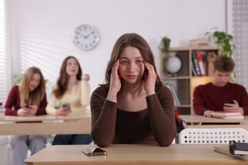 Cyber bullying. Upset teenage girl with smartphone at desk in classroom