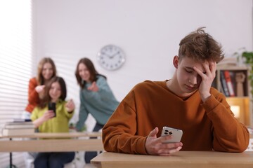 Teenage boy with smartphone suffering from bullying at school, selective focus