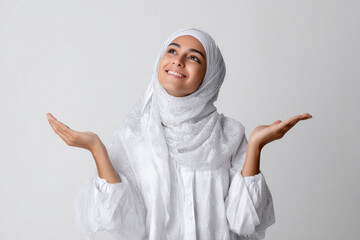 young muslim woman wearing hijab pointing with finger on white background
