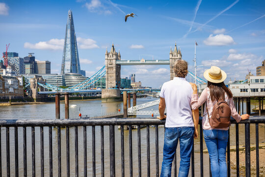 A tourist couple looks at the skyline of London, England, with Tower Bridge and Thames River during a sunny summer day