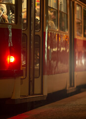A bright red and white bus is parked at a busy train station during the night, adding to the...