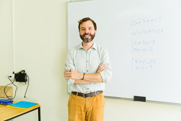 Smiling teacher standing in classroom with arms crossed by whiteboard with math equations