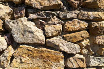 Detailed view of an old stone wall constructed from irregularly shaped, weathered rocks in earthy...
