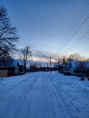 A village street completely covered with snow under the soft colors of the setting sun