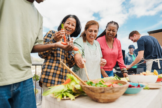 Multigenerational people doing barbecue at home's rooftop - Multiracial friends having fun eating and cooking together during weekend day - Summer and food concept - Main focus on african woman face