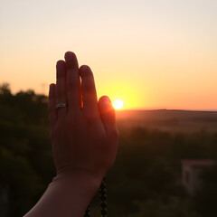 Hands in Prayer with Prayer Beads Against a Golden Sunset Background