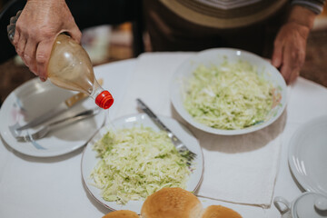 A senior woman drizzling oil over plates of shredded cabbage salad, set on a dining table alongside bread rolls and utensils, capturing a moment of meal preparation.