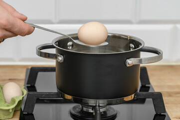 Cook putting a chicken egg with a spoon into boiling water, cooking hard-boiled eggs, soft-boiled...
