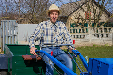 farmer in a hat with a walk-behind tractor, young happy farmer on a new tractor sits