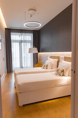 Elegant hotel room featuring two single beds, warm wooden flooring, a dark accent wall, ambient lighting, a yellow chair, and a balcony door.