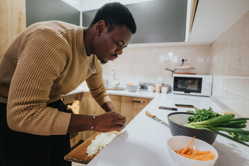 A man concentrating on chopping vegetables while preparing a dish in the kitchen, showcasing culinary skills in a home environment