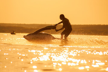 strong man jumps on the jetski above the water at sunset .silhouette spray.