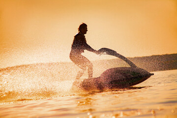 strong man jumps on the jetski above the water at sunset .silhouette spray.