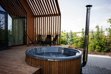 Outdoor wooden hot tub near modern patio with seating and clear sky