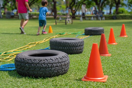 DIY obstacle course with cones, tires, ropes set up on green grass. Children playing on a grassy obstacle course with traffic cones, tires ropes, outdoor park setting, concept of outdoor fun.