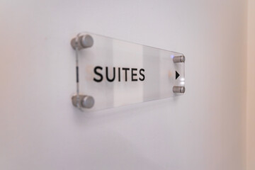 A sleek acrylic sign with bold black lettering and arrow, mounted on a white wall with metallic...