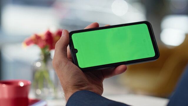 Man hand holding green screen mobile phone having video call in cafe closeup