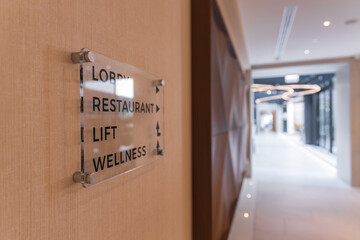 Elegant hotel hallway featuring a directional sign, wooden paneling, circular light fixtures, and natural light from large glass windows.