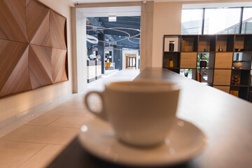 Luxurious hotel interior featuring geometric wooden wall art, large windows, curved ceiling lights, and a blurred coffee cup in the foreground.