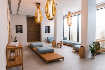 Boutique hotel spa featuring wooden furniture with blue cushions, pendant lights, potted plants, large windows, minimalist decor, and tiled flooring.