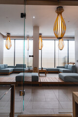 Luxury hotel spa area with light blue sofas on a wooden platform, wooden pendant lights, frosted windows, and a glass partition for an airy ambiance.