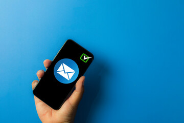  A person's hand holding a mobile phone showing a email envelope and a checkmark icon on blue background with copyspace.,Concept for message delivery confirm,digital communication,email security.