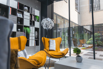 Luxurious hotel interior featuring mustard yellow armchairs, a sculptural lamp, sleek shelving, and large windows overlooking a serene courtyard.