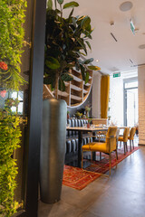 Luxurious dining space featuring a long table, mustard yellow chairs, tufted bench, red patterned rug, green wall, and natural light from large windows.