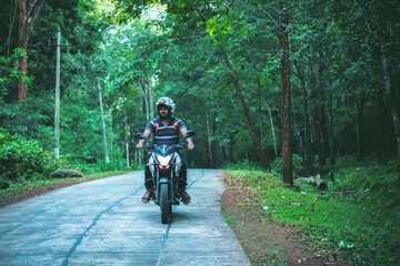 View of a young man riding a motorcycle on a forest road.