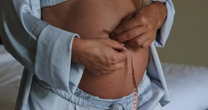 Close-up of a pregnant woman's big belly, measuring her belly with an inch tape. Weight gain during pregnancy, monitoring the health of a pregnant woman.