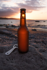 Beer bottle with opener on rock at beach during sunset